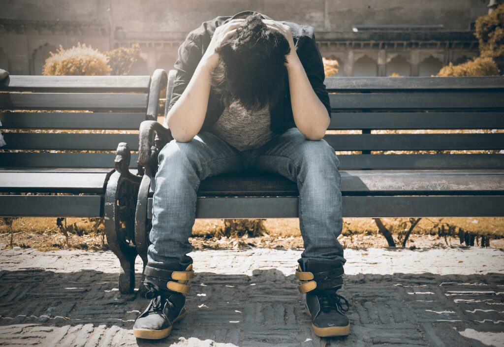 teen sitting alone on a bench with his head in his hands