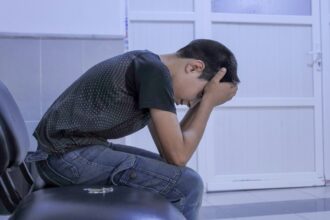 a teen sitting alone with his head in his hands looking overwhelmed
