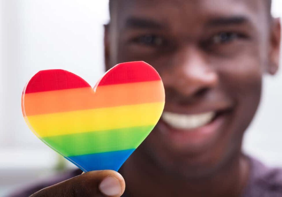 Smiling Man Holding Rainbow Heart In His Hand Against White Background